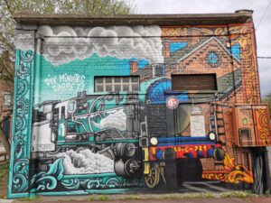 Ancien poste de transformation électrique recouvert d'une fresque murale représentant une locomotive à vapeur et en arrière plan la gare de Roncq.