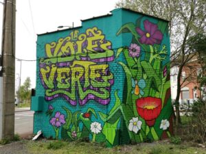 Fresque murale au dos du vieux poste de transformation électrique représentant des fleurs et de la verdure et un grande inscription en lettres arts modernes : La Voie Verte